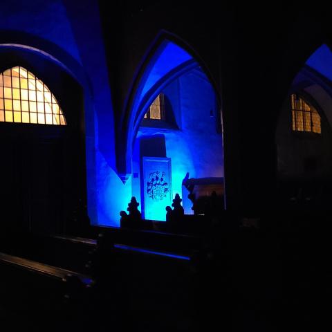 "ein großes Grabmal an der Kirchenwand, blau angestrahlt, in der dunklen Kirche"