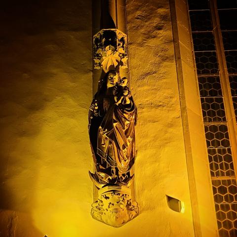 "Maria mit Jesuskind auf einem Sockel an der Wand, von unten gelb angestrahlt"
