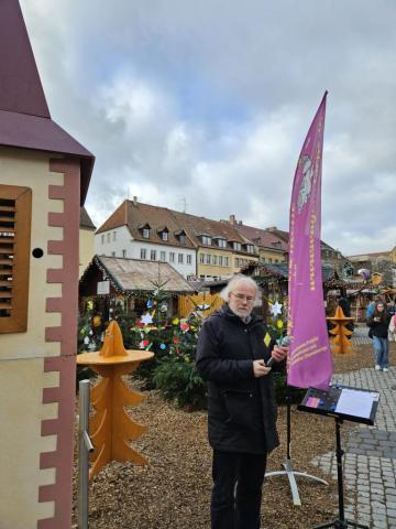 Lorenz Hummel steht mit Mikrofon zwischen Wagenkirche und der Beachflag der Wagenkirche auf dem Weihnachtsnmarkt.