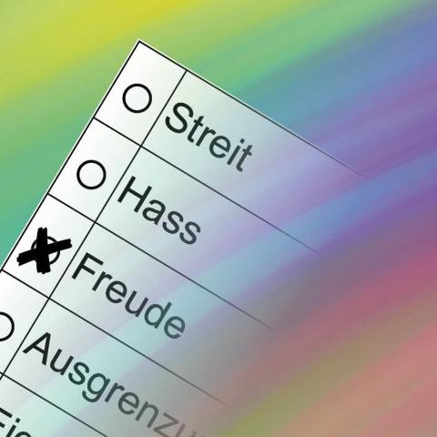 Ein bunter Farbverlauf. Eine Art Wahlzettel mit Auswahlmöglichkeiten Streit, Hass, Freude, Ausgrenzung, Eigennutz und einem weiteren Wort, das nicht komplett lesbar ist. 