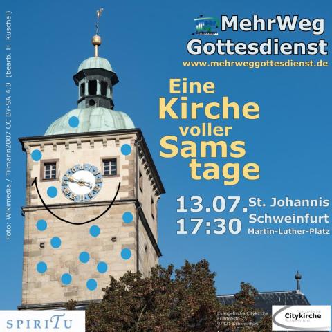 Der Turm der St. Johanniskirche Schweinfurt vor blauem Himmel. Die Kirchturmuhr sieht aus wie eine Nase zwischen den zwei Fenstern als Augen. Darunter ist mit einem Strich ein Mund angedeutet. Die Kirche ist übersät mit kleinen blauen Punkten.