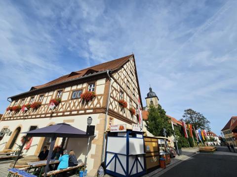 Das alte Gochsheimer Rathaus, ein imposanter Fachwerkbau. Im Hintergrund ragt der Kirchturm von St. Michael empor. Vorne eine Fischbude vom Kirchweihbetrieb.