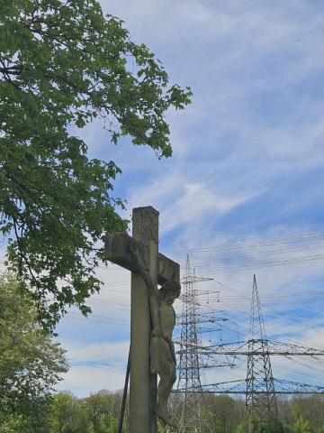 Wegkreuz aus Stein, im Hintergrund Bäume und Hochspannungsleitungen