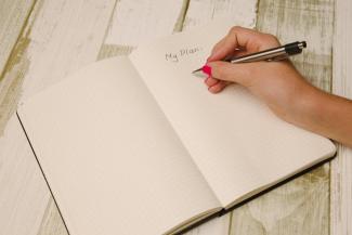 eine Hand schreibt in ein leeres Notizbuch "my plan"