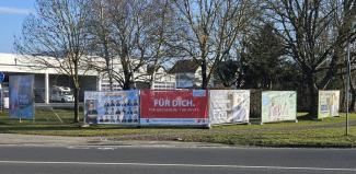 Bauzäune mit Bannern verschiedener Parteien direkt nebeneinander am Straßenrand