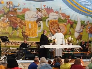 Heiko Kuschel und Ullrich Göbel in liturgischen Gewändern prosten sich auf der Volksfestbühne mit Maßkrügen zu.